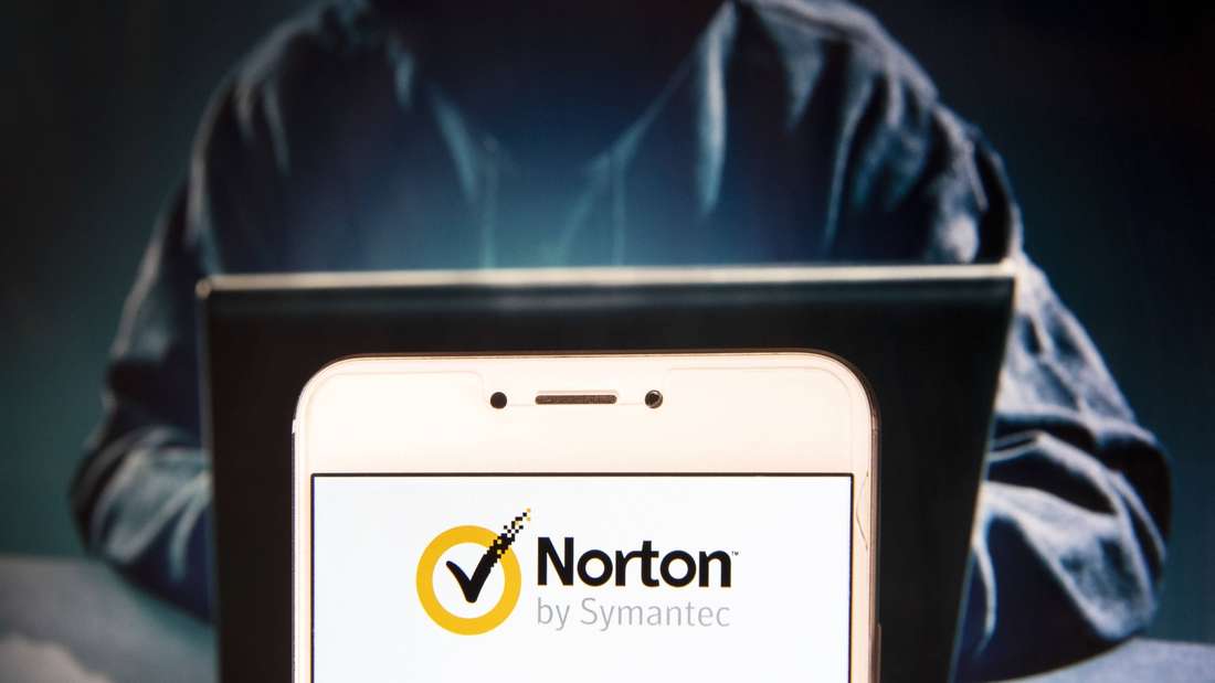 Das Logo von Norton Symantec AntiVirus auf einem Smartphone, dahinter die anonyme Figur eines Hacker