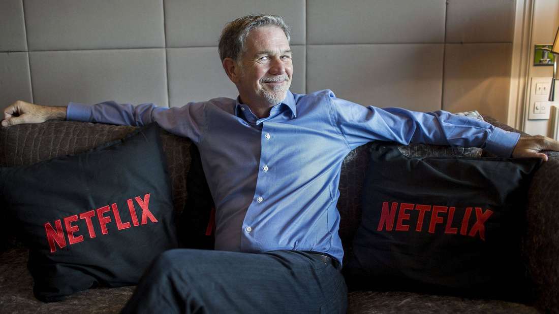 Reed Hastings sitzt auf einer Couc, die Kissen sind mit dem Netflix-Schriftzug bestickt.